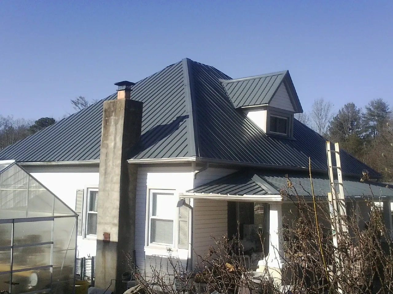 Dark blue standing seam metal roof on a white farmhouse with dormer — Slate & Tile Roof Repair by Roofing Brothers in Fleming