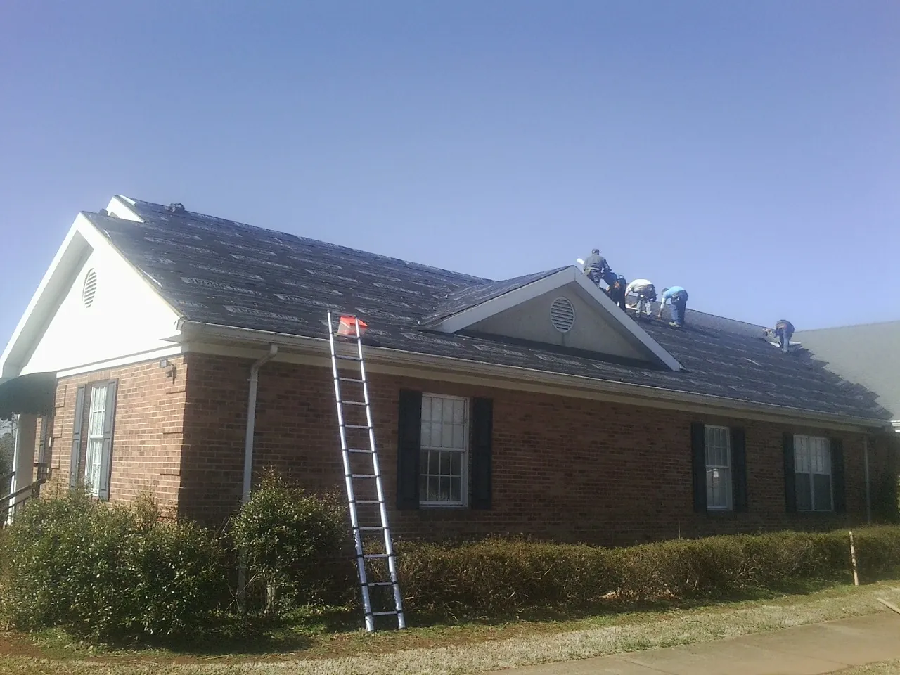 Crew tearing shingles off a brick ranch roof with a ladder set — Metal Roof Repair work by our crew in Fleming