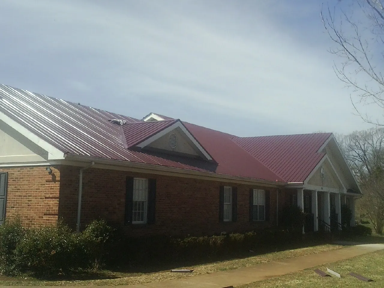 Red metal roof with gabled entries on a long brick building, from a Hail Damage Roof Repair job in Fleming