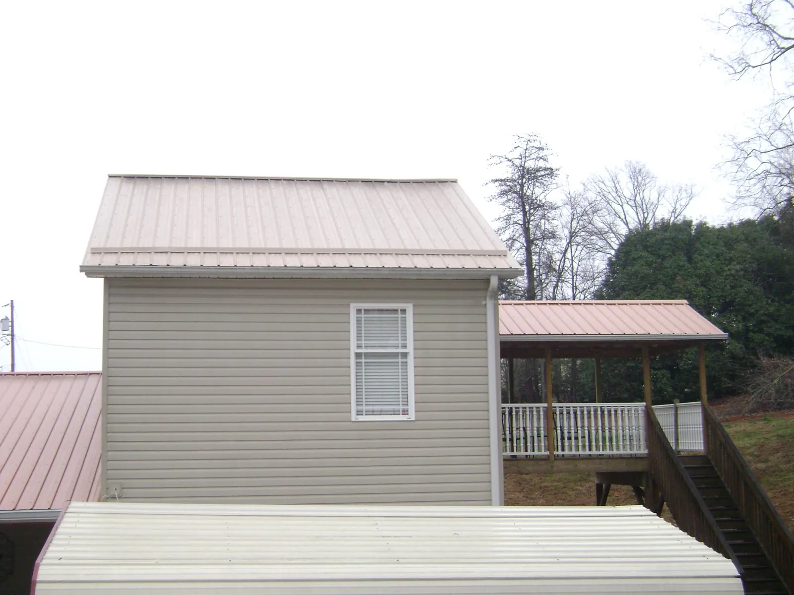 Tan metal roofs on a two story addition and attached porch, from a Roof Replacement job in Fleming